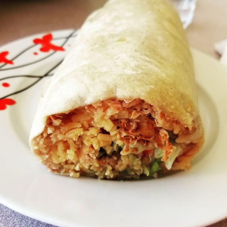 A large, golden-brown burrito from Tacontento, filled with rice and meat, on a white plate.